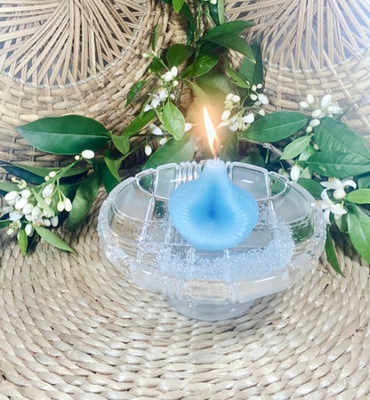 Blue Destiny Decision Candle  and orange blossoms.  The candle has a bright flame and it is placed on a round cut crystal glass pedestal dish.  The background is natural wicker. 