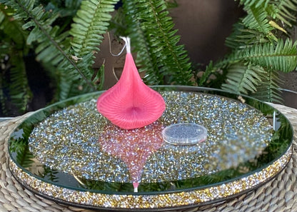 Pink candle on a reflective surface with green foliage in the background