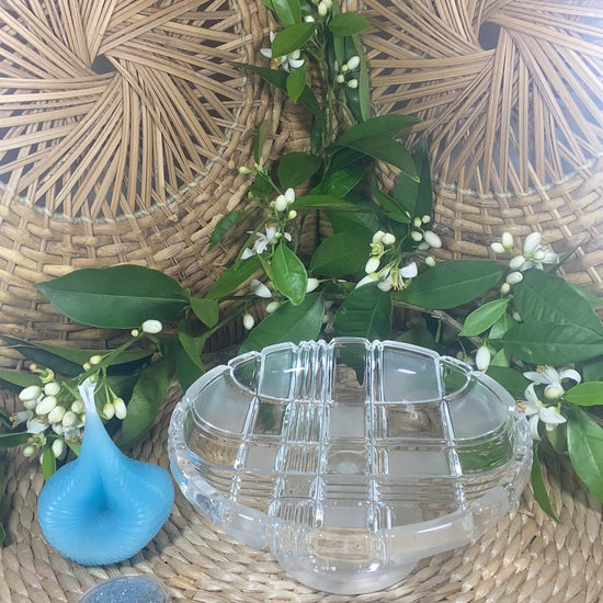 The video shows a blue Destiny Decision Candle with a round coin sized container filled with Destiny Sparkles. There is a fireproof glass plate placed on a natural wicker table and a wicker background. Green leaves and tiny Valencia orange blossoms are in the background.

Demonstrating how to use the Destiny Decision Candle.  Pour the Destiny Sparkles into the glass plate.  Place the candle candle on top of the Destiny Sparkles.  Ask your yes or no question as you light the two wicks.
